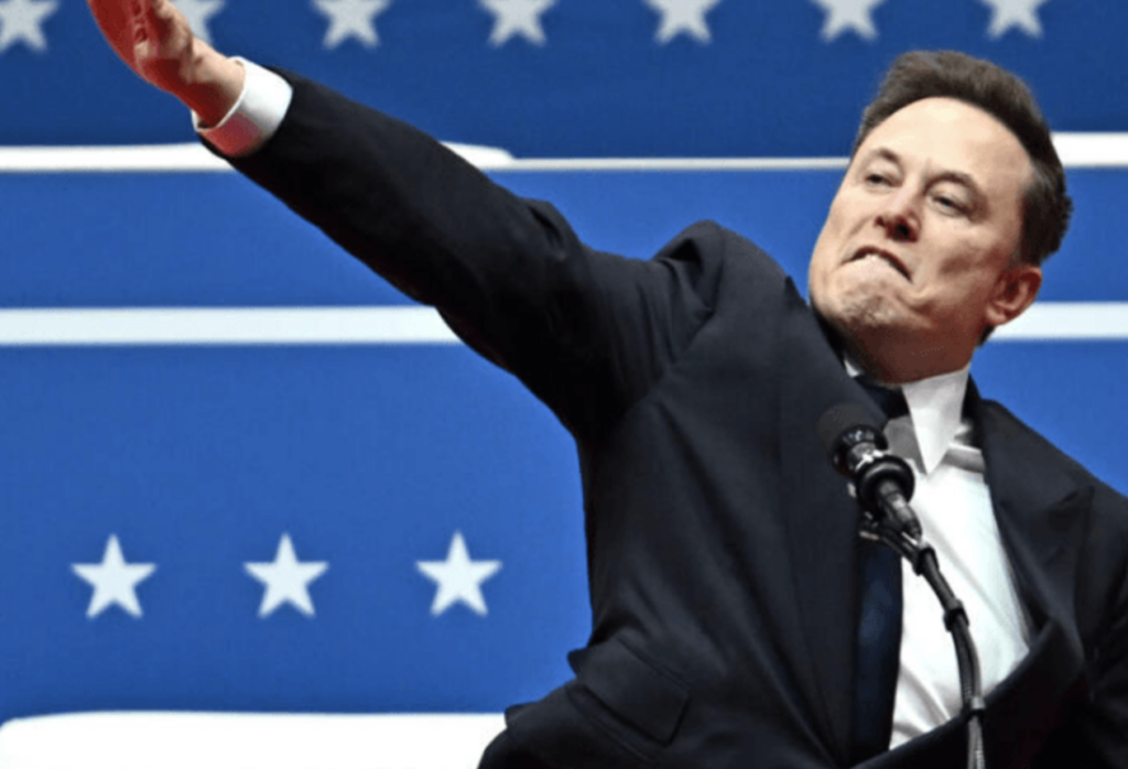 Tech billionaire Elon Musk lifts his right arm on a diagonal with palm turned down and fingers closed in a gesture similar to a Nazi salute.